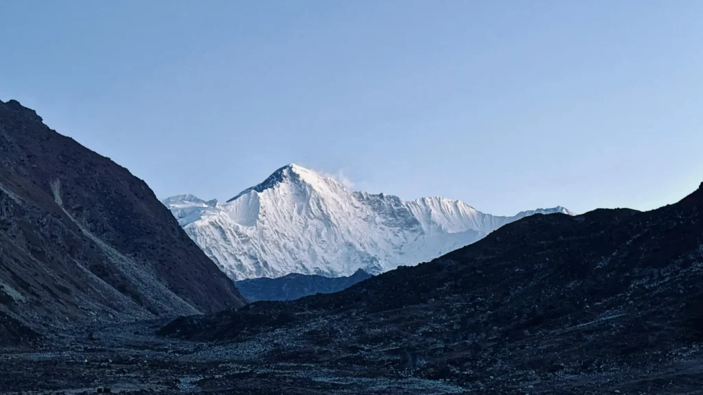 Snow-covered Makalu, the world’s fifth-highest mountain, seen at dawn between two dark, rocky ridges, under a clear blue sky.