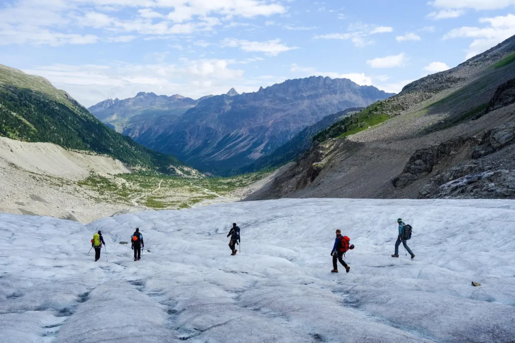 **Alt text:**
Group of climbers carefully descending a glacier with crampons, surrounded by green valleys and rugged mountain peaks under a partly cloudy sky.