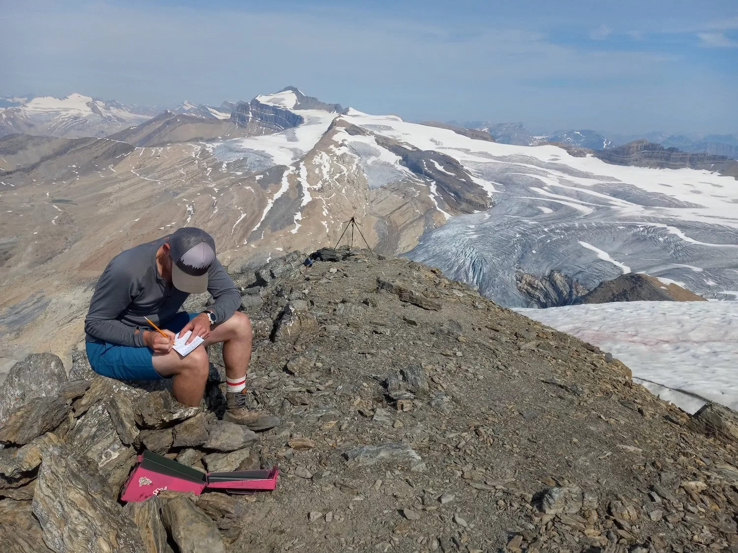 man is writing in notebook, background mountains