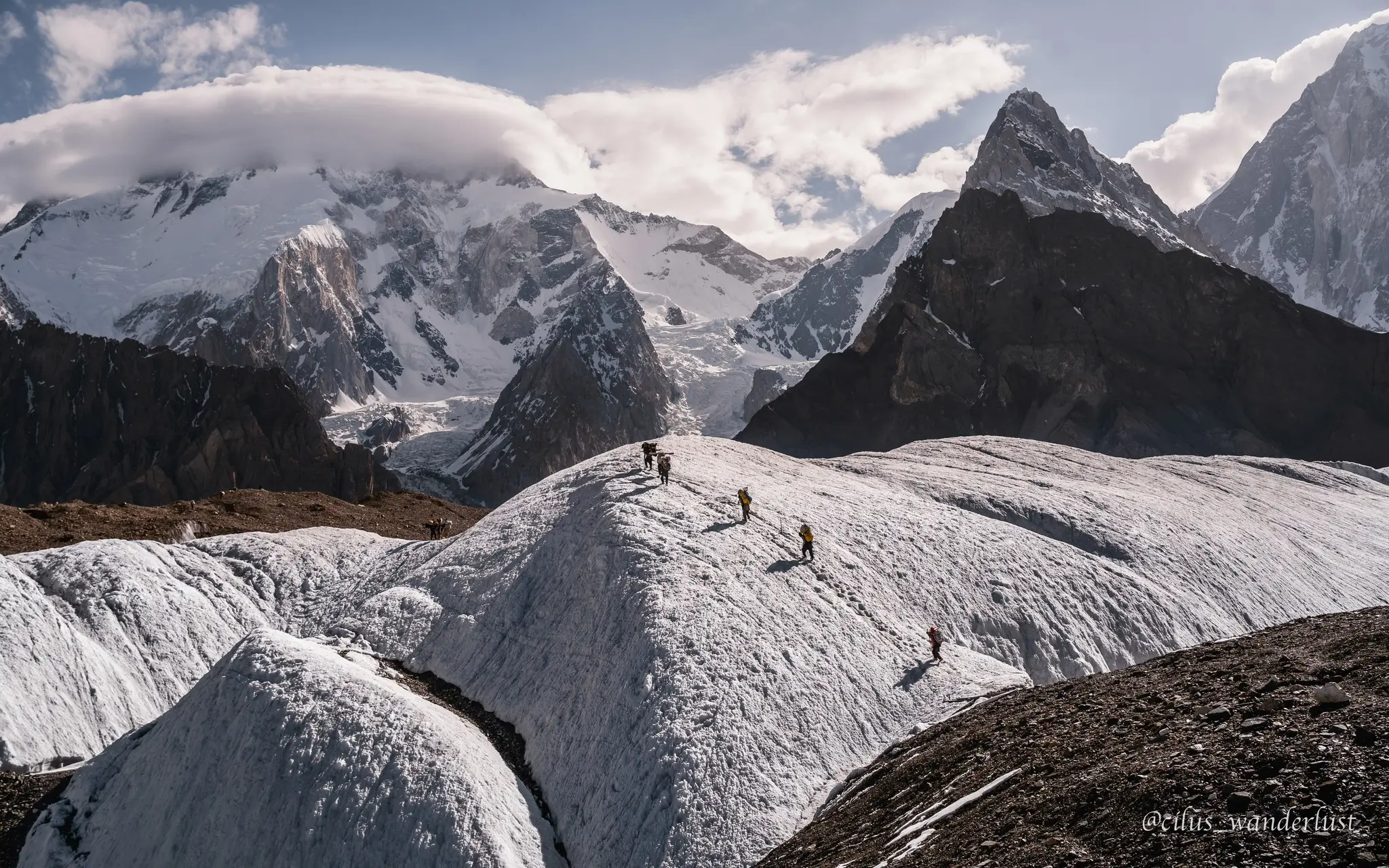 A detailed image of K2's southeast face showing the classic Abruzzi Spur route. The photo is marked with the climbing route in red, starting from K2 Base Camp at 16,500 ft and progressing through key points: Advanced Base Camp, Camp 1 (16,500 ft), Camp 2 (22,000 ft), Camp 3 (24,000 ft), Camp 4 (25,000 ft), and the summit at 28,251 ft. Landmarks such as the Black Pyramid, House’s Chimney, and Chinese Camp 1 (20,500 ft) are labeled along the ascent. The mountain is covered in snow and ice under a bright blue sky.