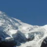 Snow-covered mountain of the Mont Blanc, with blue sky drifting below the jagged summit and a forested valley visible