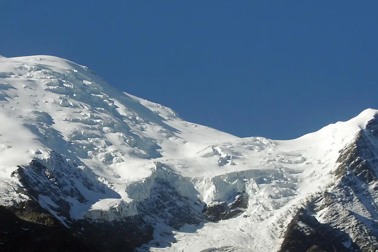 Snow-covered mountain of the Mont Blanc, with blue sky drifting below the jagged summit and a forested valley visible