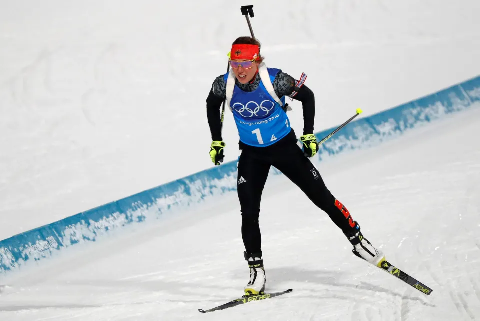 Laura Dahlmeier competes in a biathlon event at the 2018 Winter Olympics in Pyeongchang, wearing a blue Olympic bib with number 14, carrying a rifle on her back, and skiing across a snowy course in full gear.