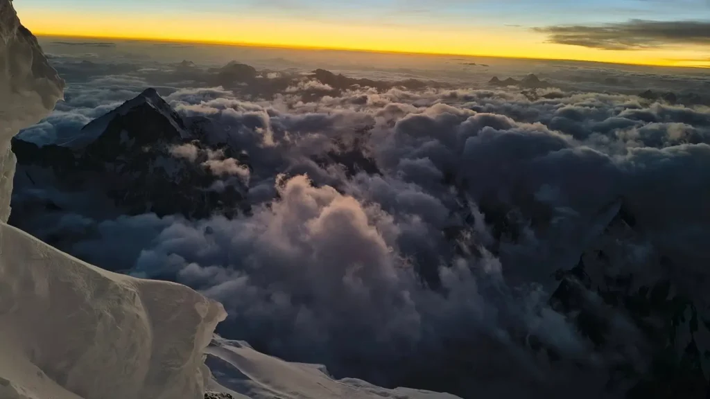 A breathtaking view of snow-covered mountain peaks rising above a sea of clouds, with a golden sunrise or sunset casting a warm glow across the horizon.