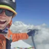 mountaineer Tyler Andrews is smiling, its his selfie on summit with background of clouds and snowy mountains