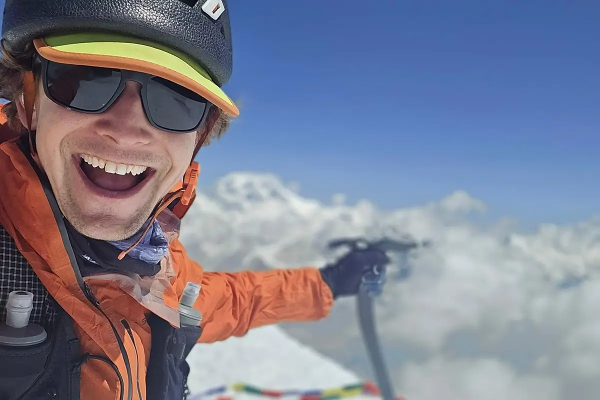 mountaineer Tyler Andrews is smiling, its his selfie on summit with background of clouds and snowy mountains