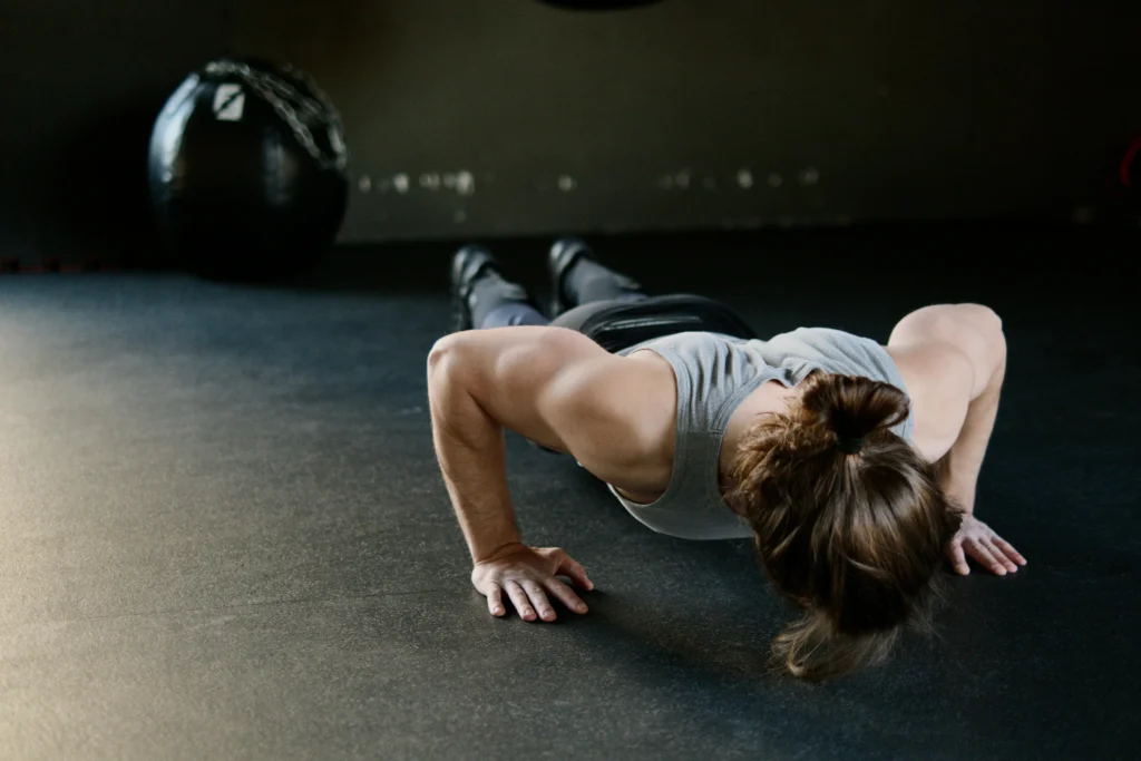 A person performing a push-up on a dark mat in a gym, with a large exercise ball and chains visible in the background.