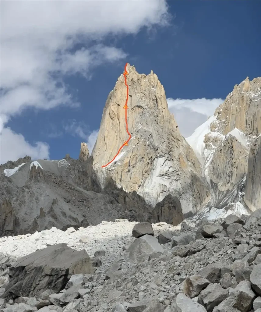 A lone climber in dark gear ascends a steep, golden-hued rock face at sunrise or sunset, with a vast glacier and towering, snow-dusted peaks stretching into the distance under a warm, glowing sky.