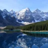 **Alt text:** *Moraine Lake in Banff National Park, with turquoise waters reflecting snow-capped Rocky Mountain peaks and dense pine forest under a clear blue sky.*