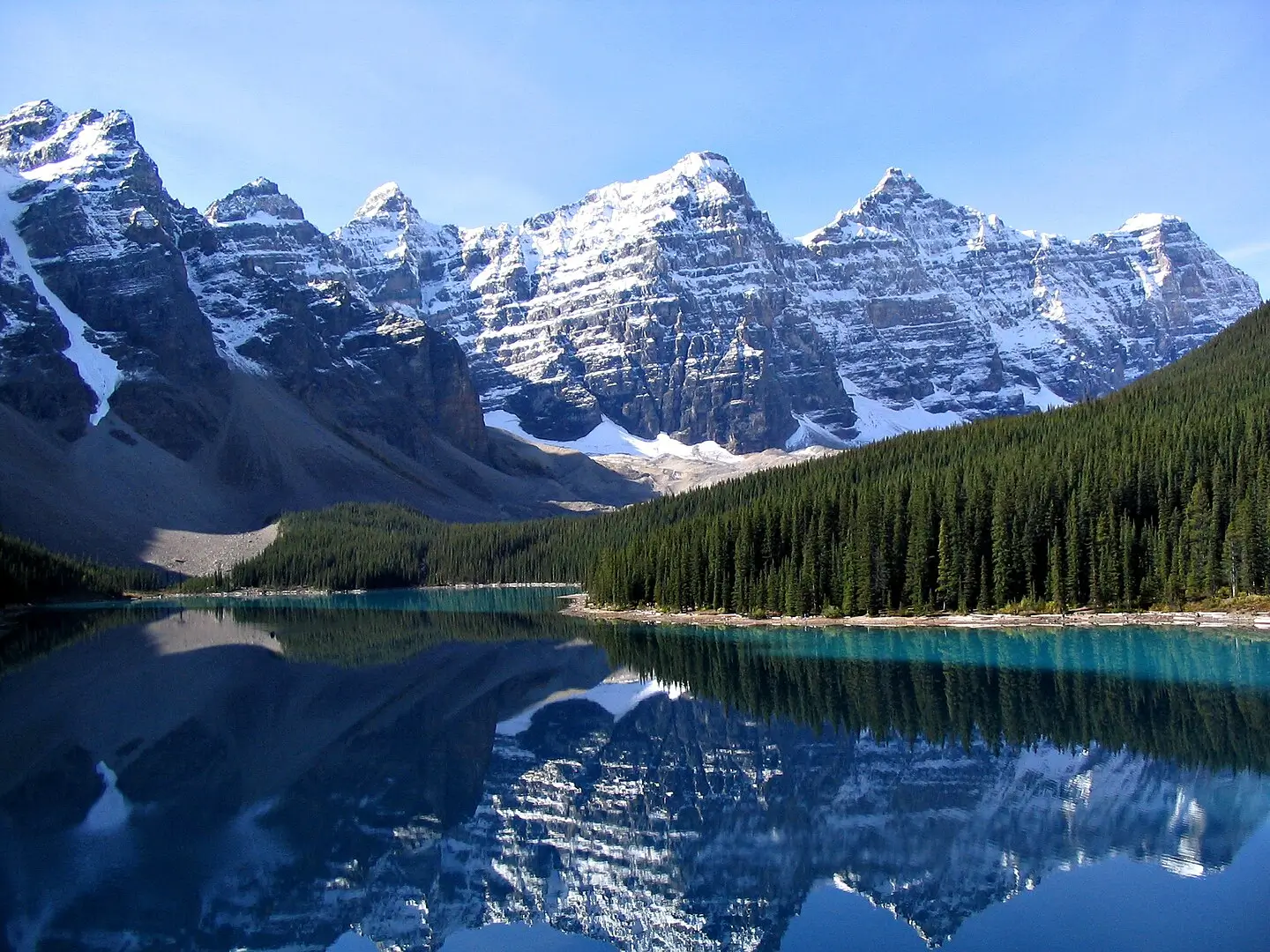 **Alt text:** *Moraine Lake in Banff National Park, with turquoise waters reflecting snow-capped Rocky Mountain peaks and dense pine forest under a clear blue sky.*